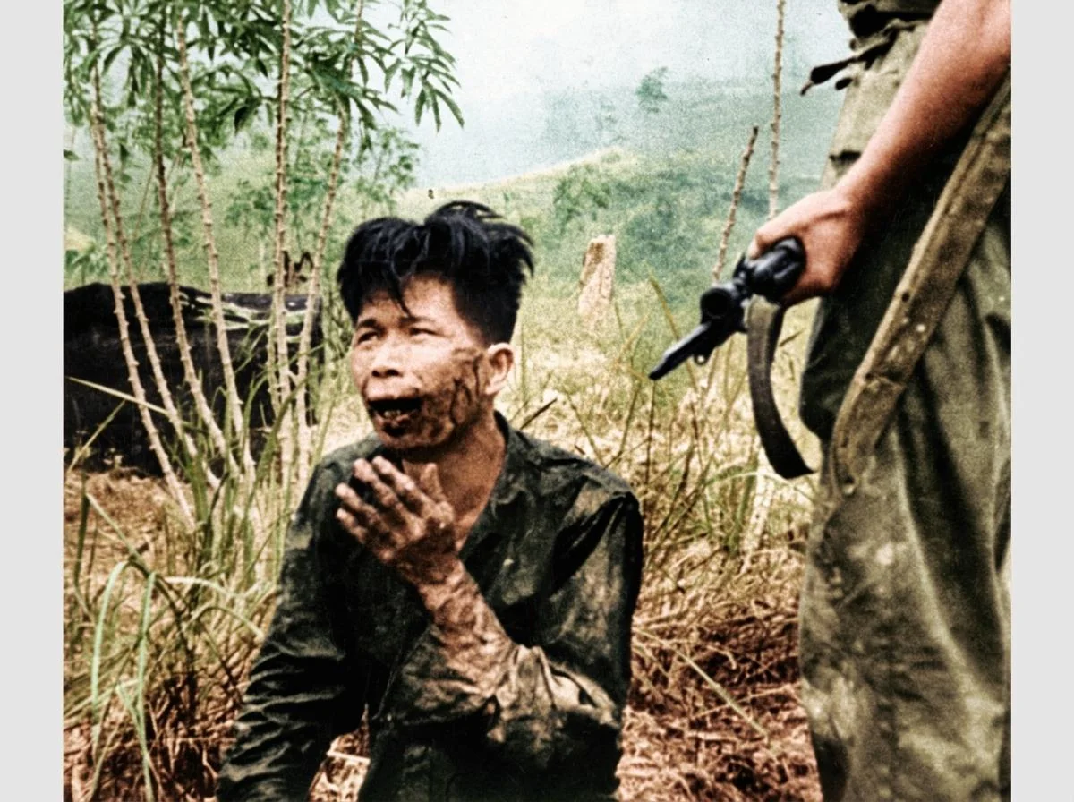 殖民军警枪口下视死如归的年轻战士历史实照（约1951–1953年）：定格反抗帝国主义暴政的钢铁意志，背景为游击军民赖以充饥生存的木薯地。        