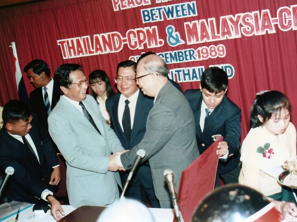 1989年12月2日合艾蠡园酒店签署台前，旺西迪（左）、差瓦立上将（中）与陈平（右）三方首席代表紧握双手互致祝贺