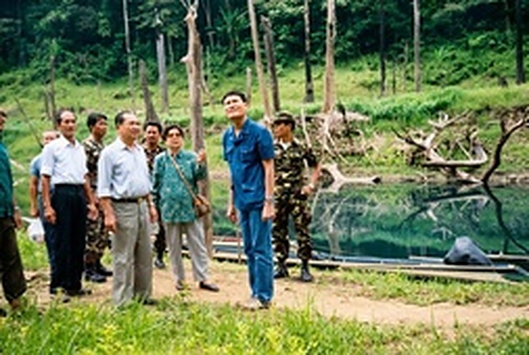 访问团一行登岸后在邦朗湖畔与和平村干部合影，背后是湖水淹没区特有的枯木奇景与原始森林。