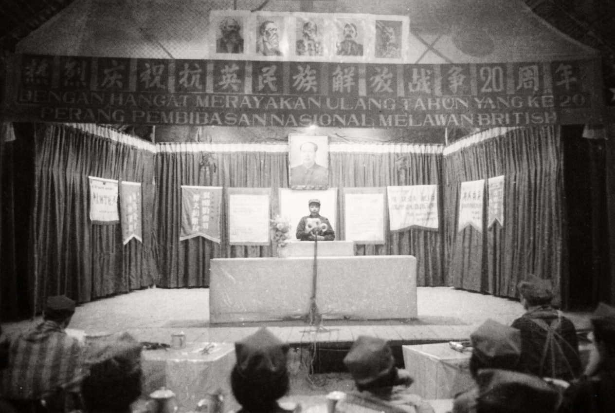 1968年6月20日密林营地悬挂的华巫双语“热烈庆祝抗英民族解放战争20周年”巨幅会标，台前陈列各支队与分区敬献的贺幛与武器模型。