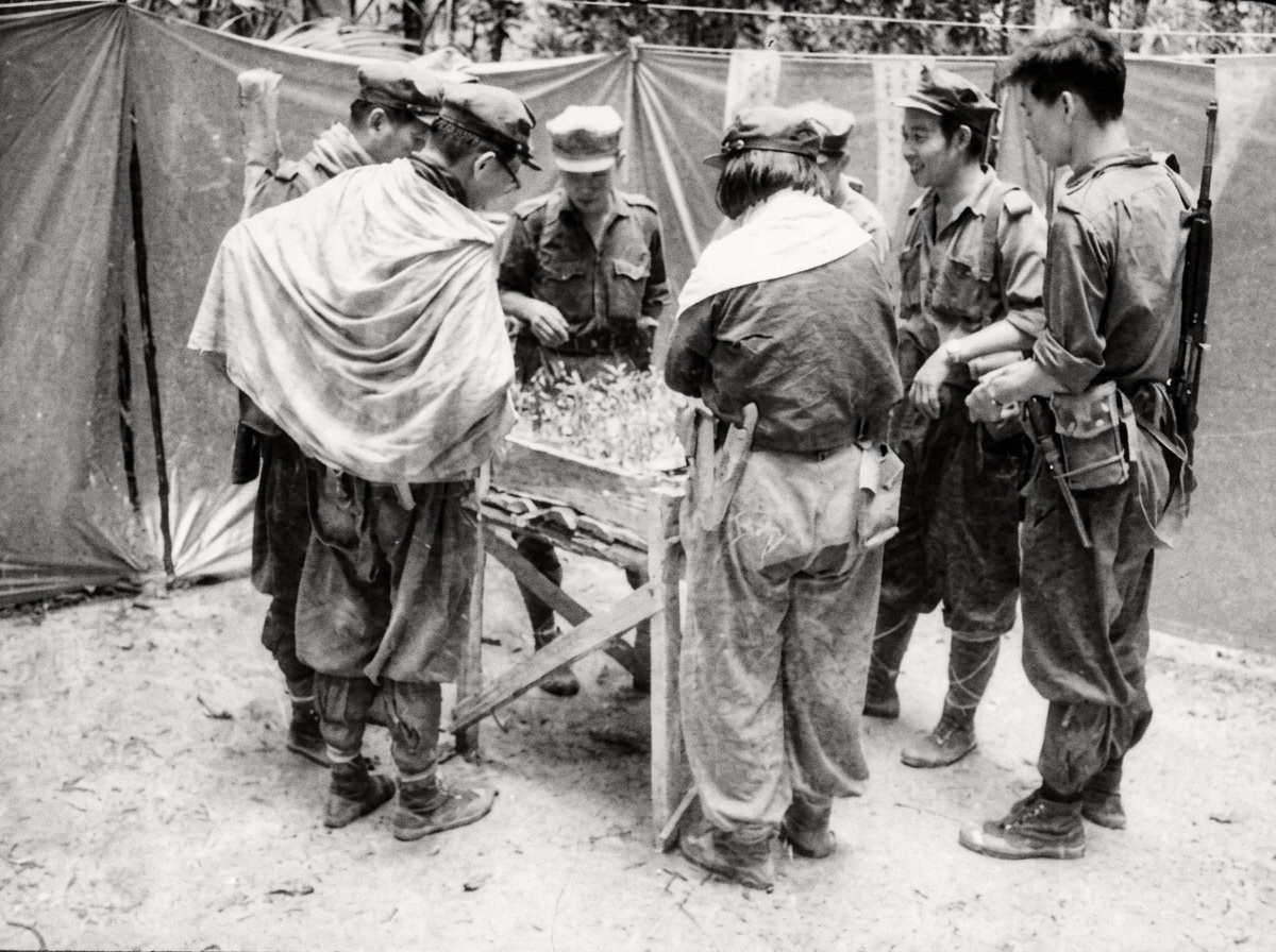 1967年密林营地军事作业展览期间，部队指挥员与战斗员围聚在山地战术沙盘模型前研讨游击战术。