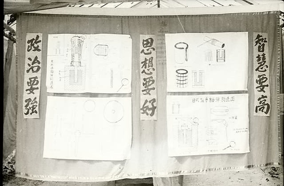 密林营地军事技术展览上悬挂的《木柄手榴弹构造图》与《日式型号手榴弹构造图》手绘工程图谱，两侧书写“政治要强、思想要好、智慧要高”标语。