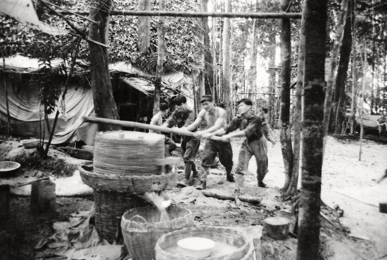 1967年密林大本营内，后勤与民运战士合力推动自制竹木磨谷机加工稻谷，保障深山部队的粮食供应。